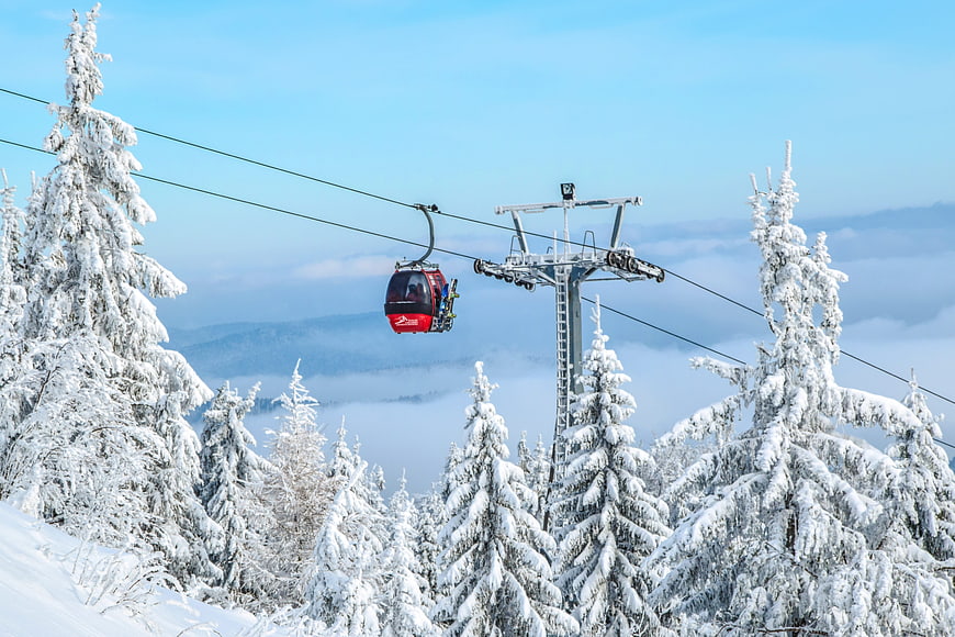 Red Gondola Lift Above Snowy Pine Trees And Mountain Clouds