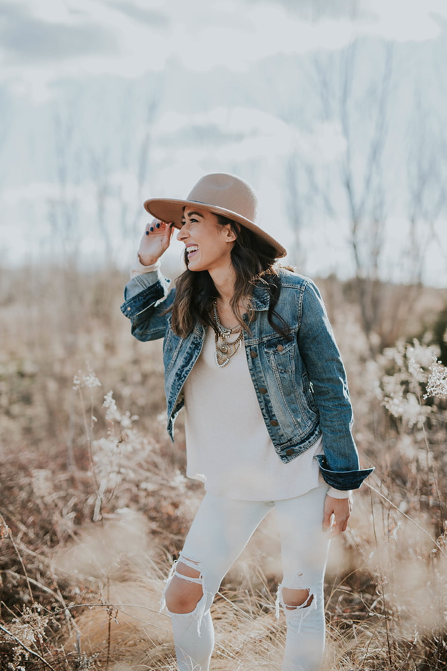 Happy woman in denim jacket and hat laughing in field