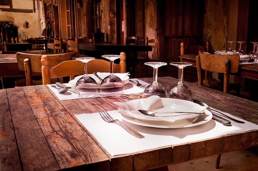 Rustic wooden table set with white plates and wine glasses in a restaurant