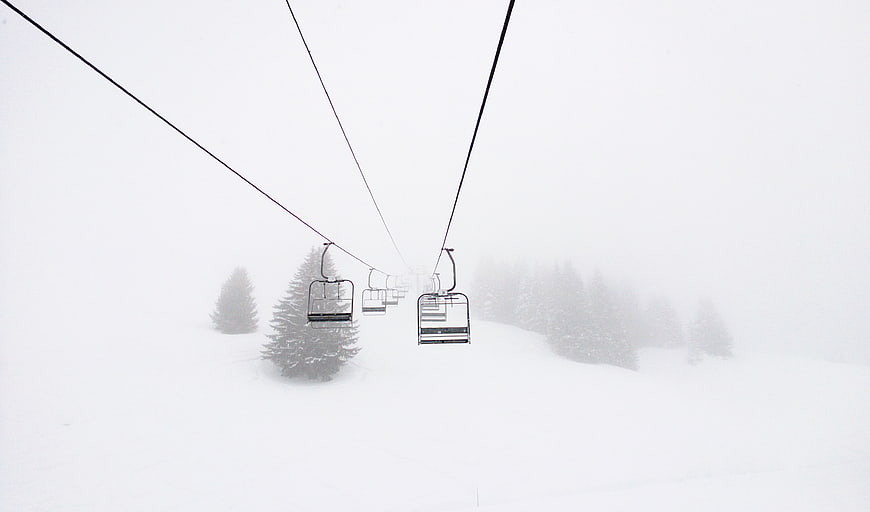 Empty ski lift chairs disappearing into whiteout fog
