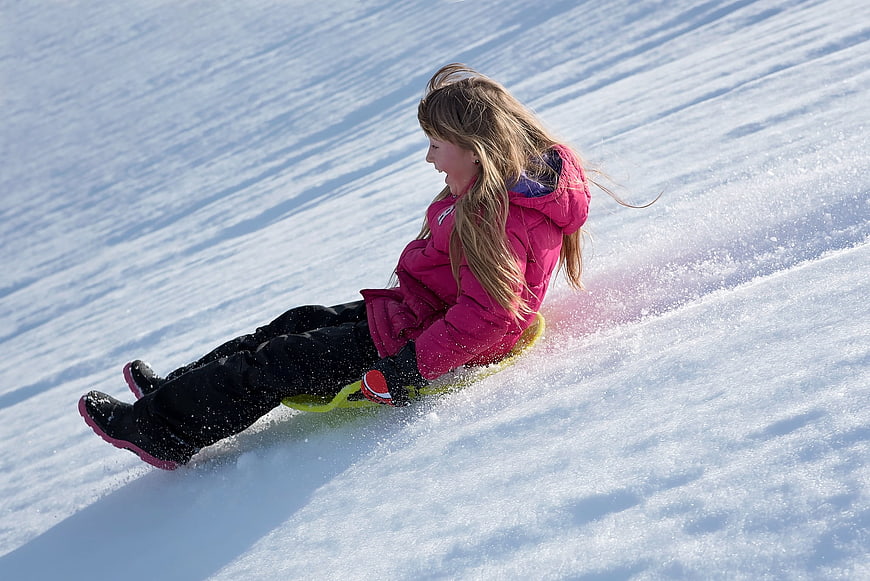 Happy Girl Sledding Down Snowy Hill in Winter
