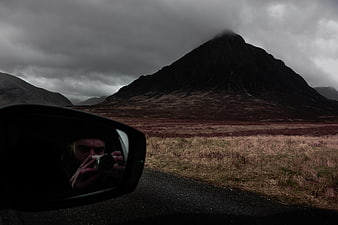 Photographer Reflection in Car Mirror Against Dark Mountain