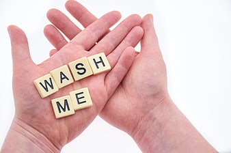 Hands holding Scrabble tiles spelling wash me on white background