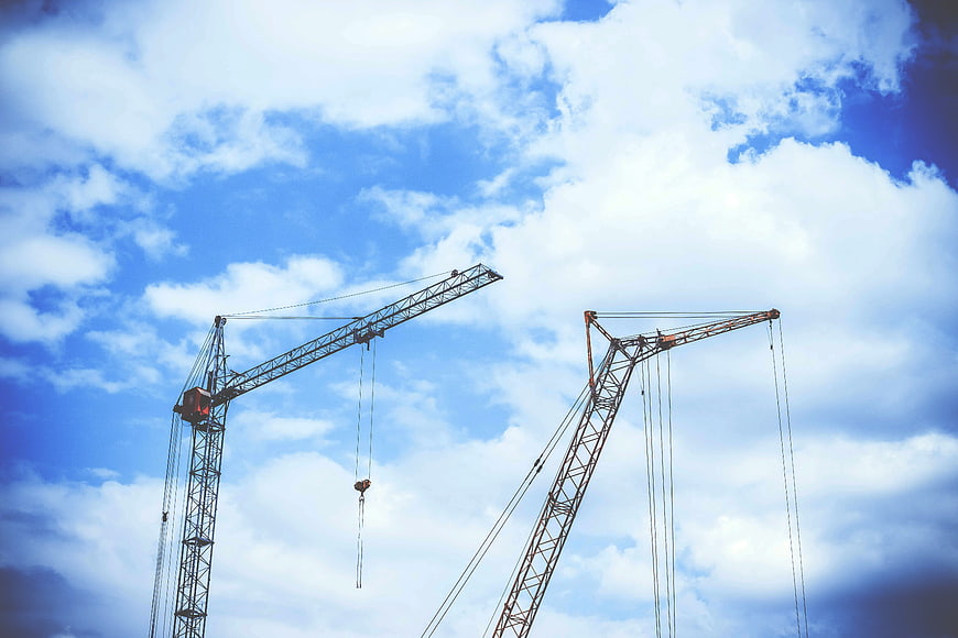 Two Construction Cranes Against Blue Sky with Clouds