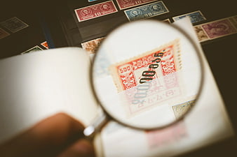Close-up of magnifying glass inspecting vintage postage stamps