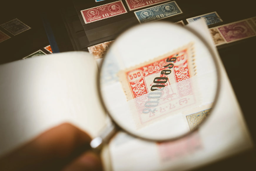 Close-up of magnifying glass inspecting vintage postage stamps