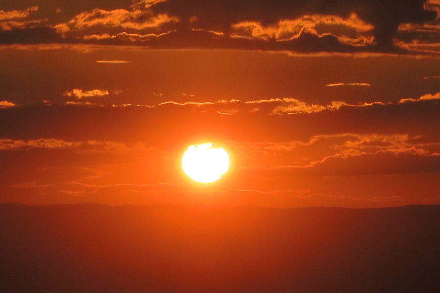 Vibrant orange sunset with bright sun and clouds over mountains