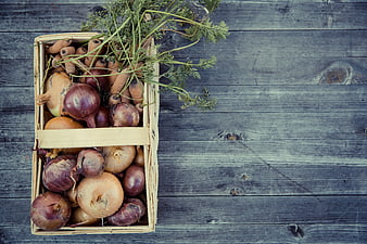 Top view of wooden crate with fresh onions and carrots on rustic wood
