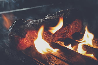 Close-up of a thick steak grilling over open flames on a barbecue grate