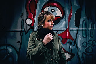 Woman in Green Jacket Standing Against Colorful Graffiti Wall