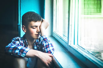 Teenage boy resting head on hand by window