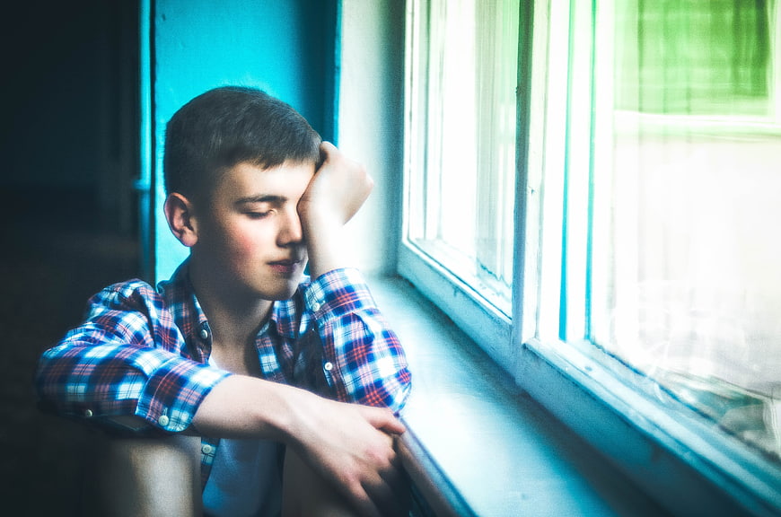 Teenage boy resting head on hand by window