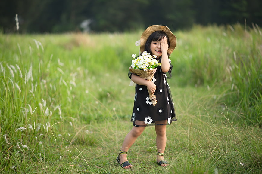 Smiling young girl in straw hat holding white flowers in green field