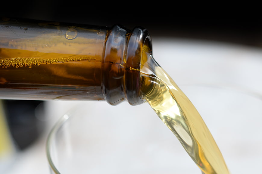 Close-up of golden beer pouring from a brown glass bottle