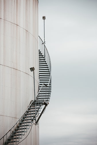 Curved metal staircase on industrial silo against gray sky