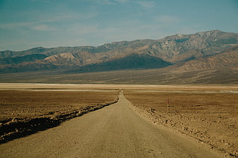 Desolate dirt road leading to mountains in desert landscape