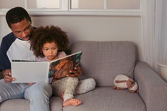 Father and daughter reading a book together on a couch