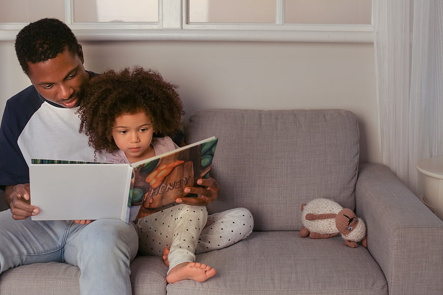 Father and daughter reading a book together on a couch