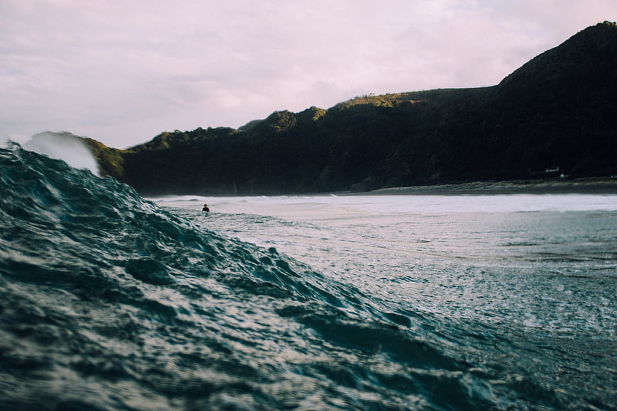 Dramatic Ocean Wave Crashing Near Dark Forested Hills