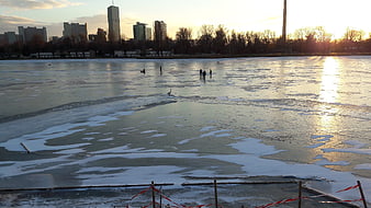 Wide view of frozen lake with city skyline at sunset