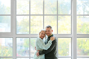 Senior couple hugging affectionately in front of a large window