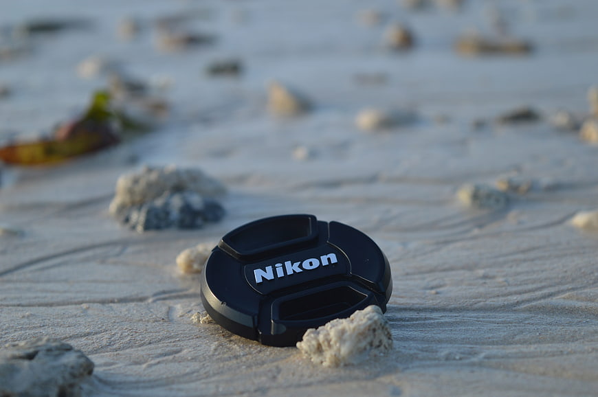 Black Nikon lens cap on white sand beach