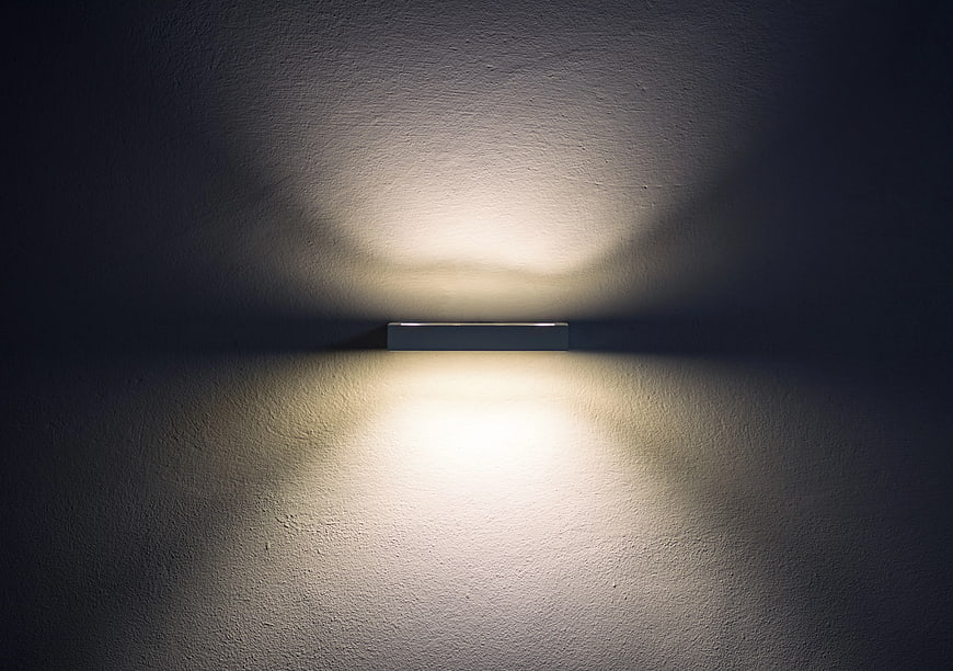 Modern wall sconce casting symmetrical light on textured wall
