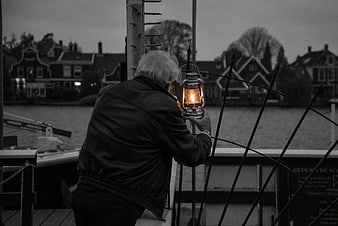 Senior man holding glowing lantern on boat deck at dusk