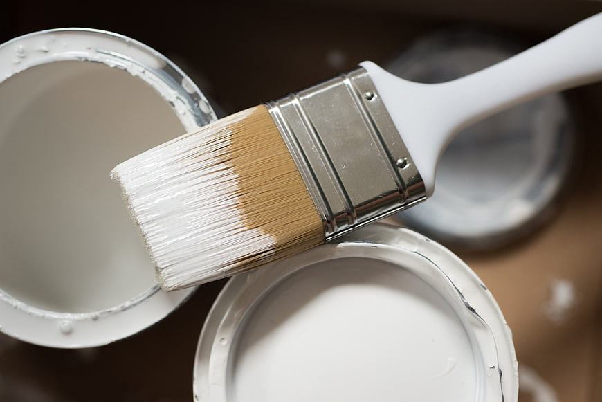 White paintbrush dipped in paint can close-up
