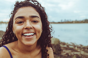 Close-up portrait of smiling woman with curly hair by the sea