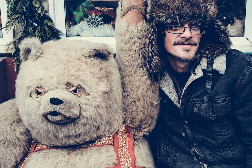 Man in fur hat posing with large bear mascot