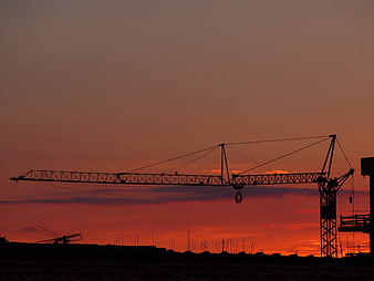 Silhouette of Construction Crane Against Vibrant Orange Sunset Sky