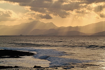 Golden sunset rays over ocean waves and distant mountains