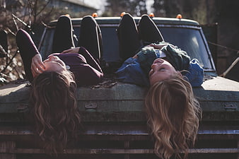 Two happy women laughing while lying on an old truck hood