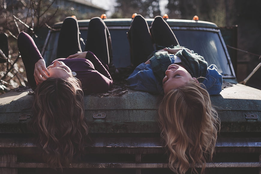 Two happy women laughing while lying on an old truck hood