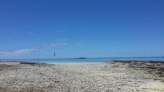 Wide shot of rocky beach with blue sky and distant boats
