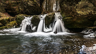 Frozen waterfall cascading over mossy rocks in winter forest