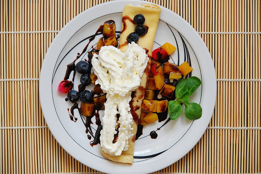 Overhead view of rolled pancake with whipped cream and fruit