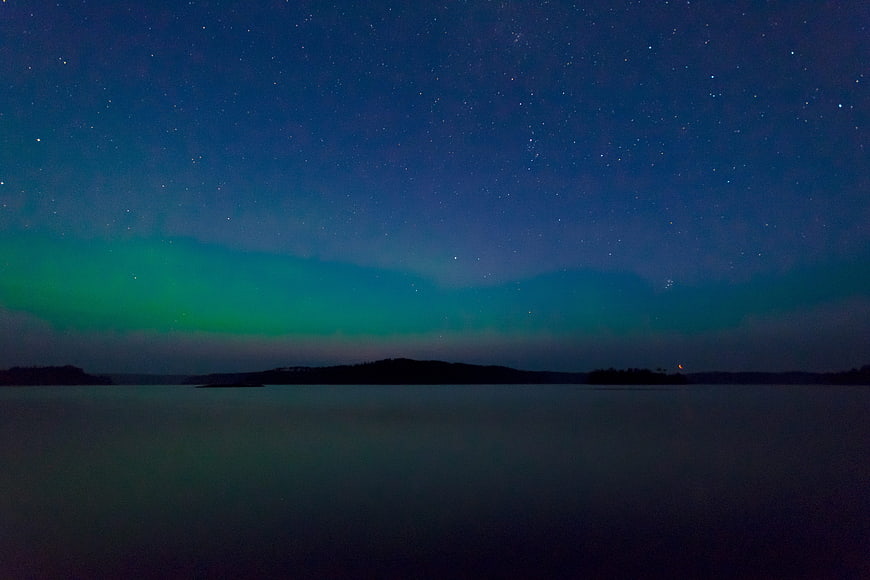 Aurora Borealis over a calm lake at night with stars