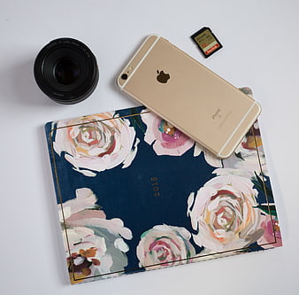 Flat lay of gold iPhone, camera lens, and floral planner on white background