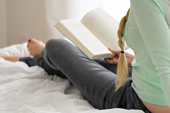 Woman Reading Book in Bed with White Linens
