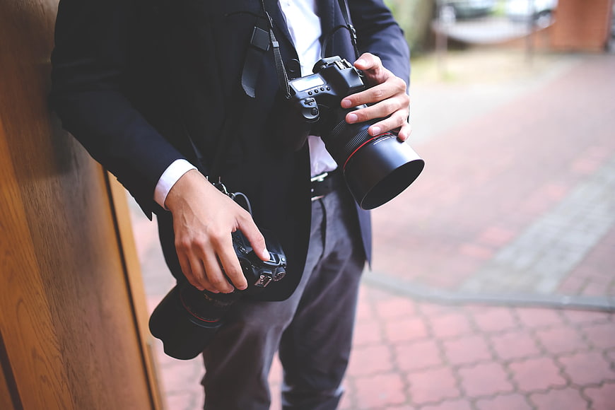 Professional photographer holding two DSLR cameras in suit