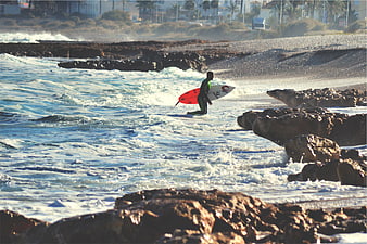 Surfer with Red Board Walking Through Rocky Ocean Waves