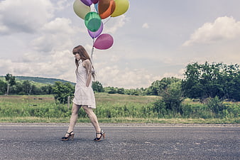 Woman in White Dress Walking with Colorful Balloons on Road