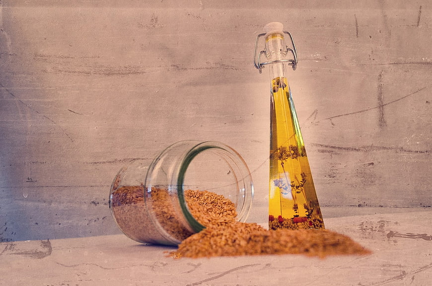 Glass bottle of infused oil and spilled seeds on rustic wooden background