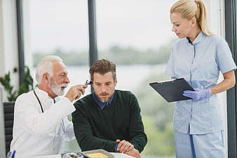 Doctor examining patient's ear with nurse observing