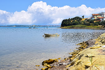 Small boat anchored in calm coastal waters near rocky shore