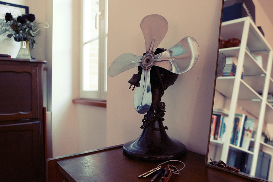 Vintage metal fan on wooden table with keys and mirror