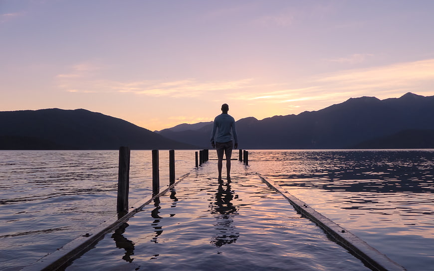 Man Standing on Submerged Wooden Pier at Sunset