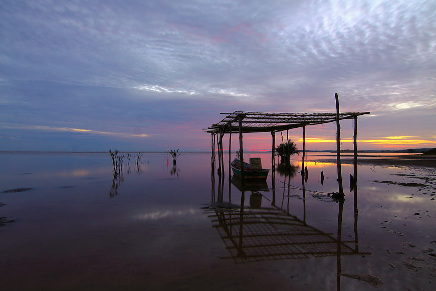 Silhouette of wooden shelter and boat at sunset on calm beach
